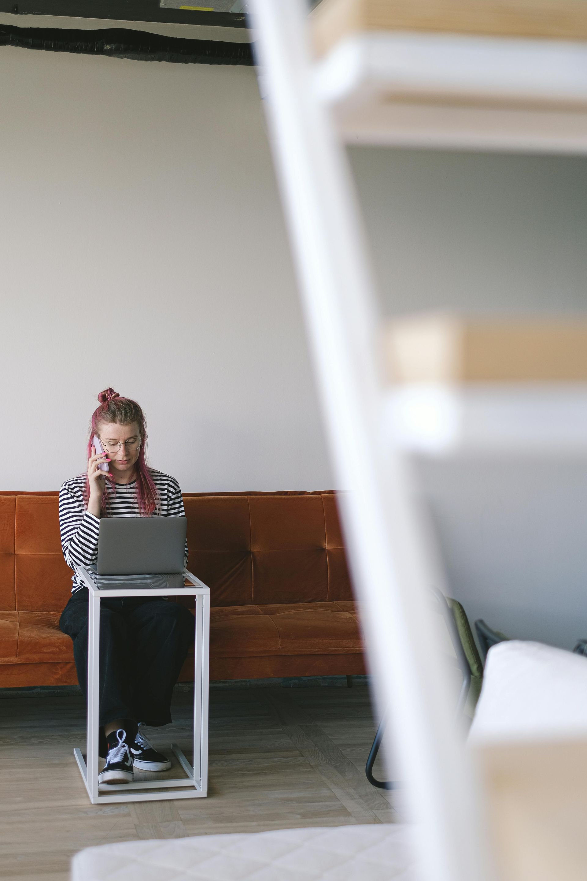 A woman is sitting on a couch using a laptop and talking on a cell phone.