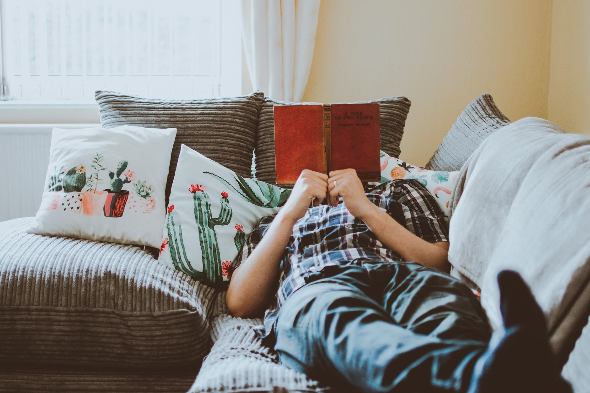 A person is laying on a couch reading a book.