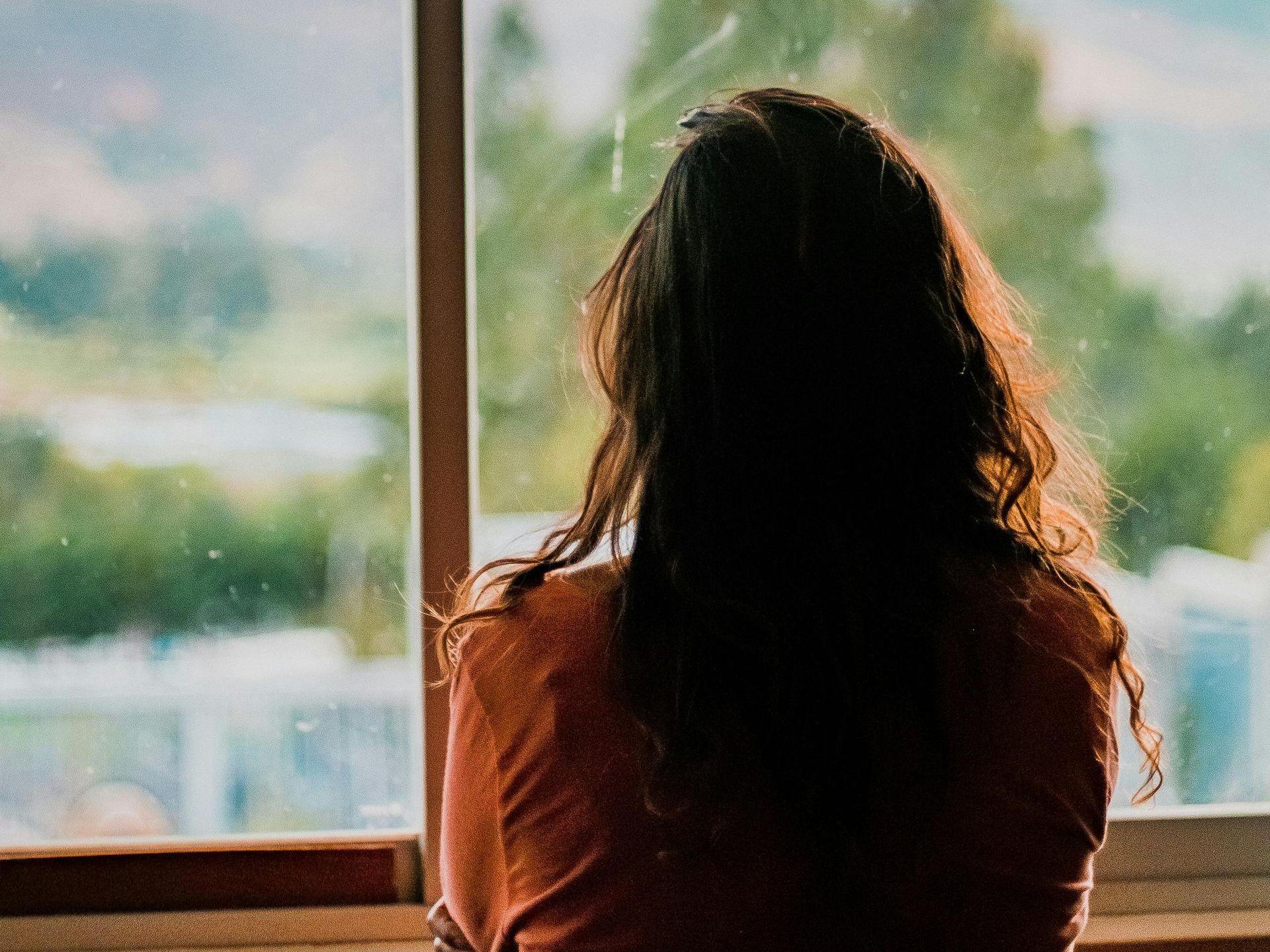 A woman is sitting in front of a window looking out.