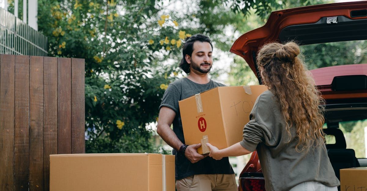 A man is carrying a cardboard box to a woman in a car.