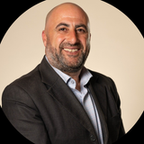 A bald man with a beard is wearing a suit and smiling.