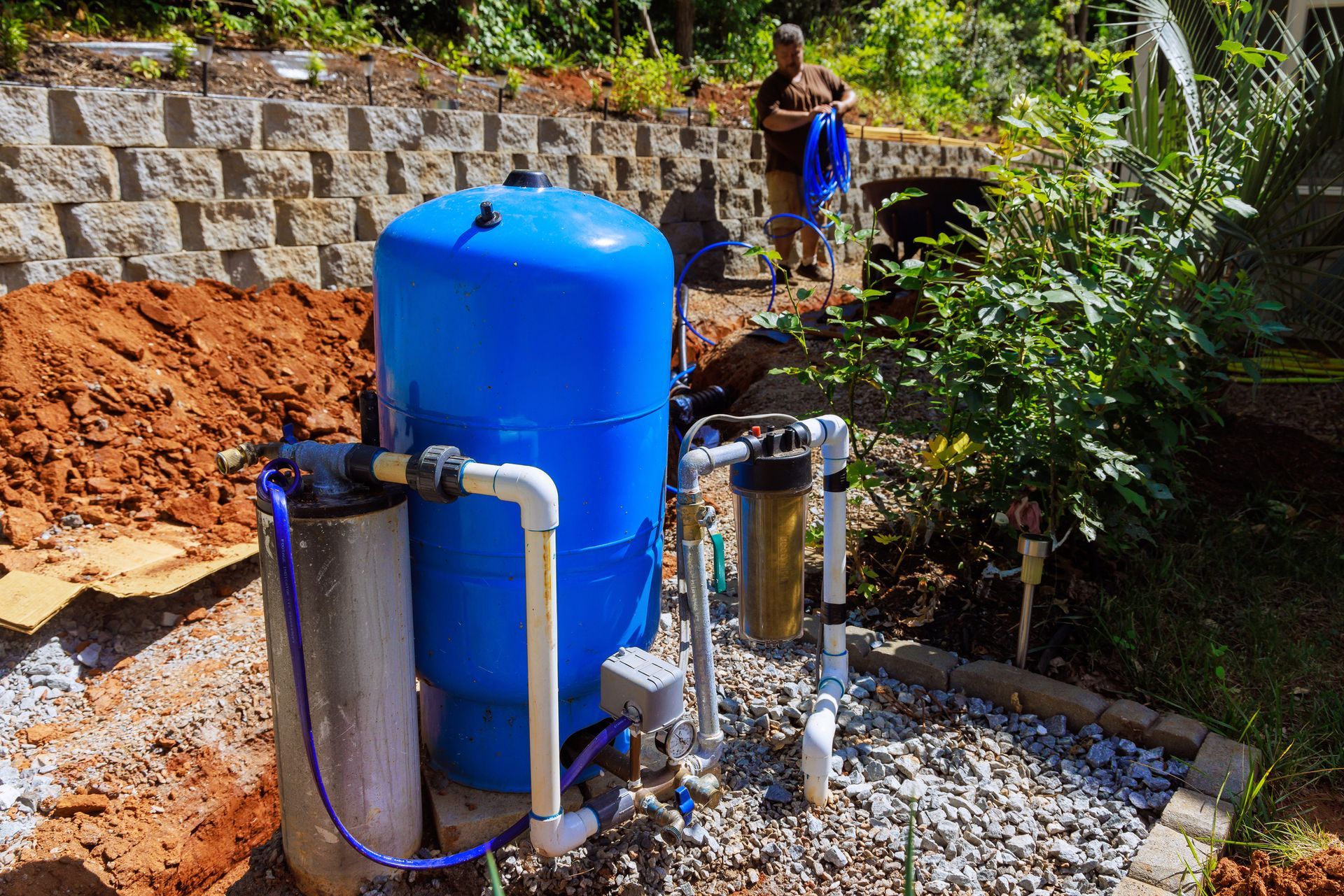 Water well pump contractor installing blue pressure tank and filters in backyard water system.