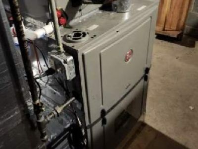 Furnace unit in a basement setting, gray and metallic, with pipes and electrical components.