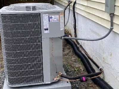 An air conditioning unit outside a building, with copper pipes and electrical wiring.
