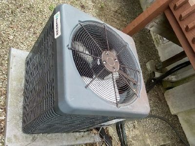 Gray outdoor air conditioner unit with fan, next to a deck.