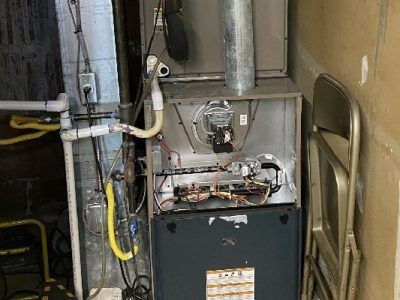 A furnace in a utility room, with open panels revealing internal components and ductwork.