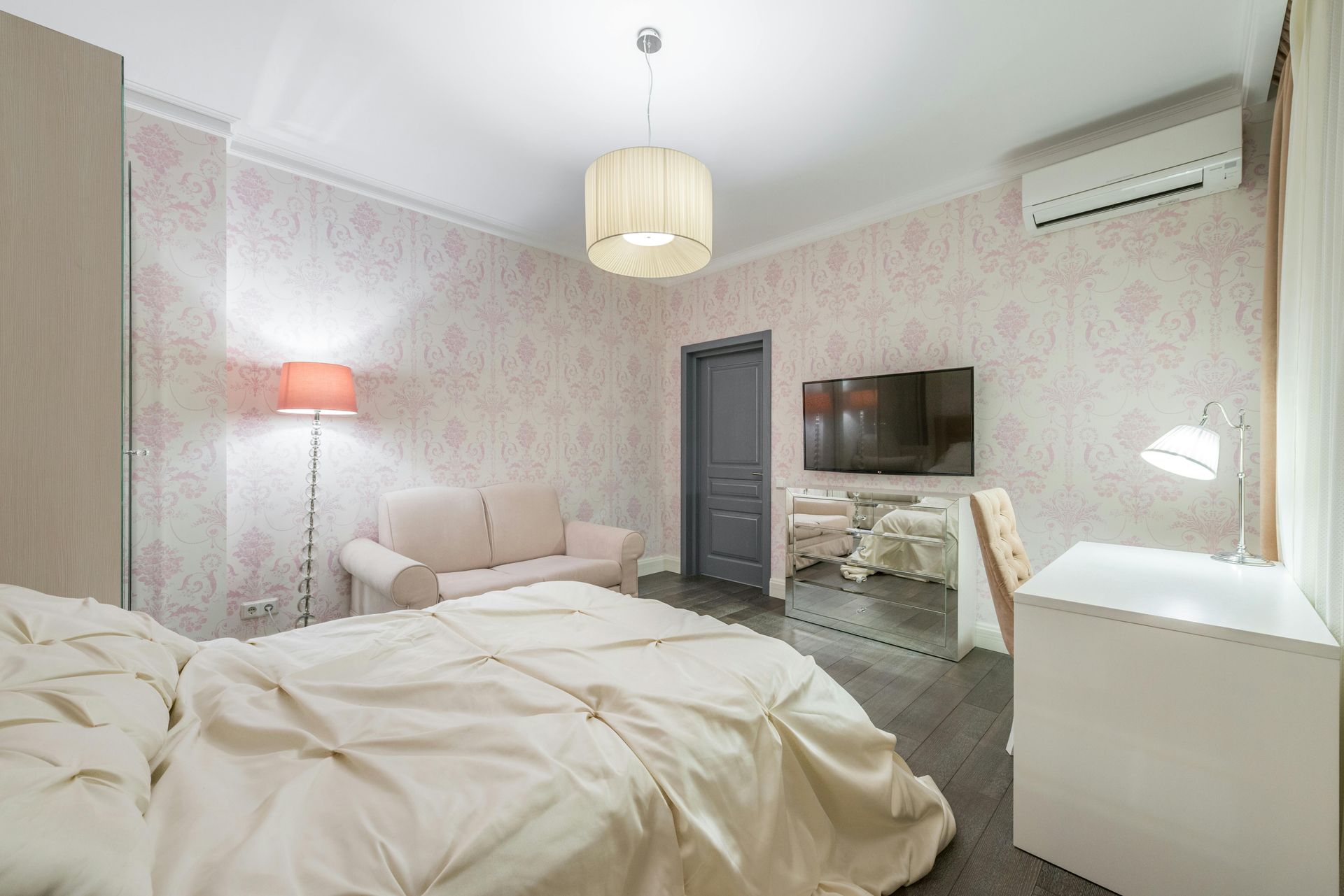 Bedroom with bed, sofa, desk, TV, floral wallpaper, and neutral colors.