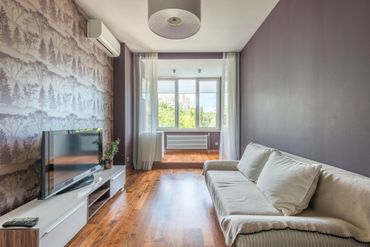 Living room with a landscape wallpaper accent wall, purple walls, white sofa, TV, and large window.