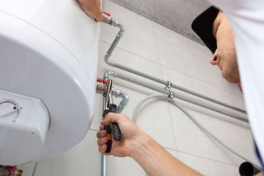 Plumber using wrench to connect pipes to a white water heater in a bathroom.