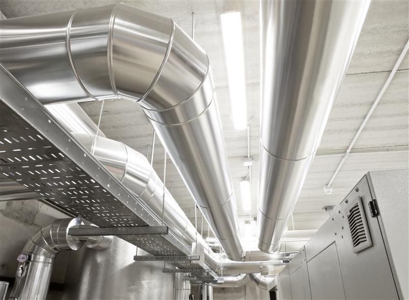 Silver HVAC ducts and electrical conduits on a ceiling in an industrial setting.