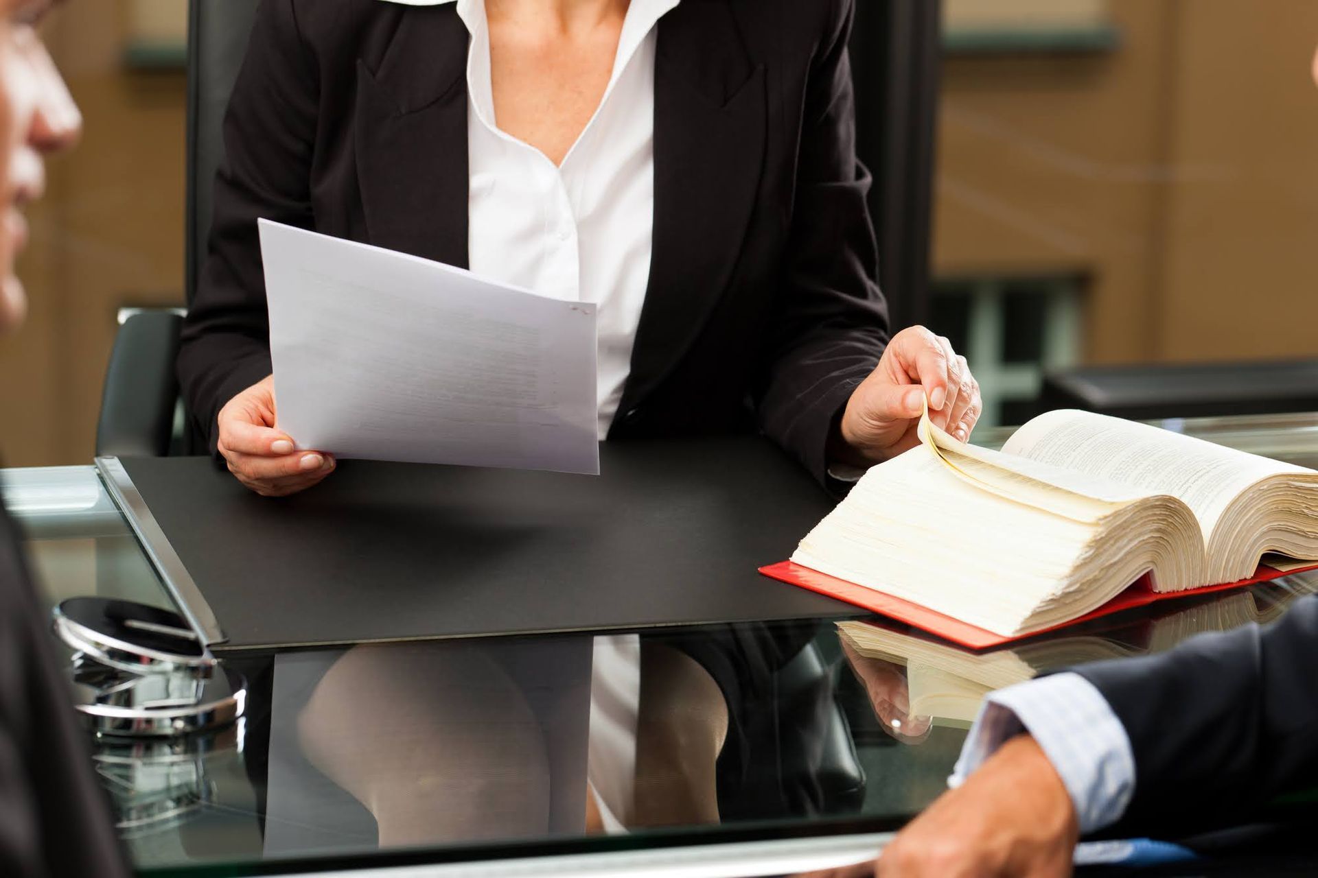 A woman is sitting at a desk holding a piece of paper and a book.