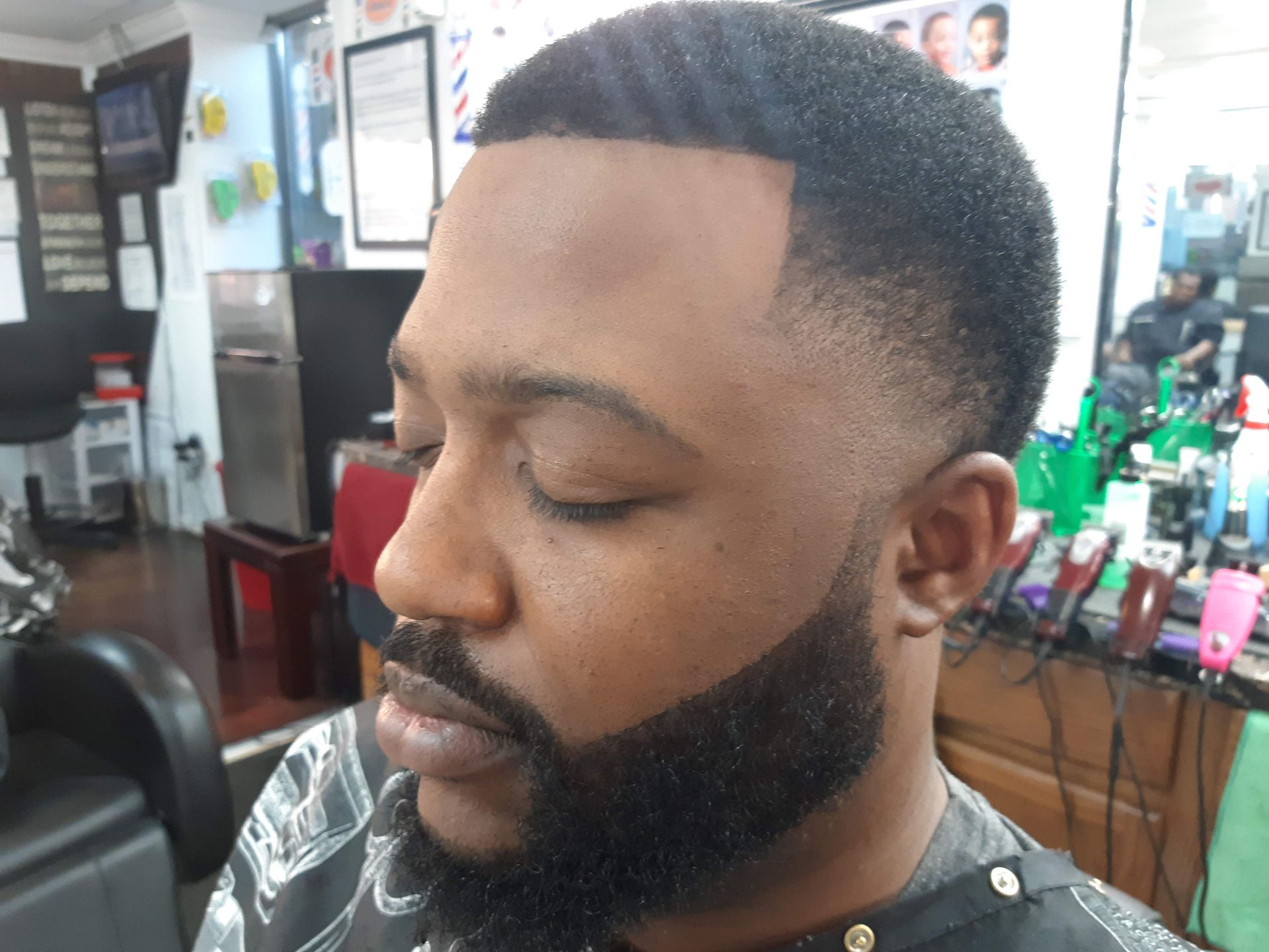A man with a beard is getting his hair cut at a barber shop.