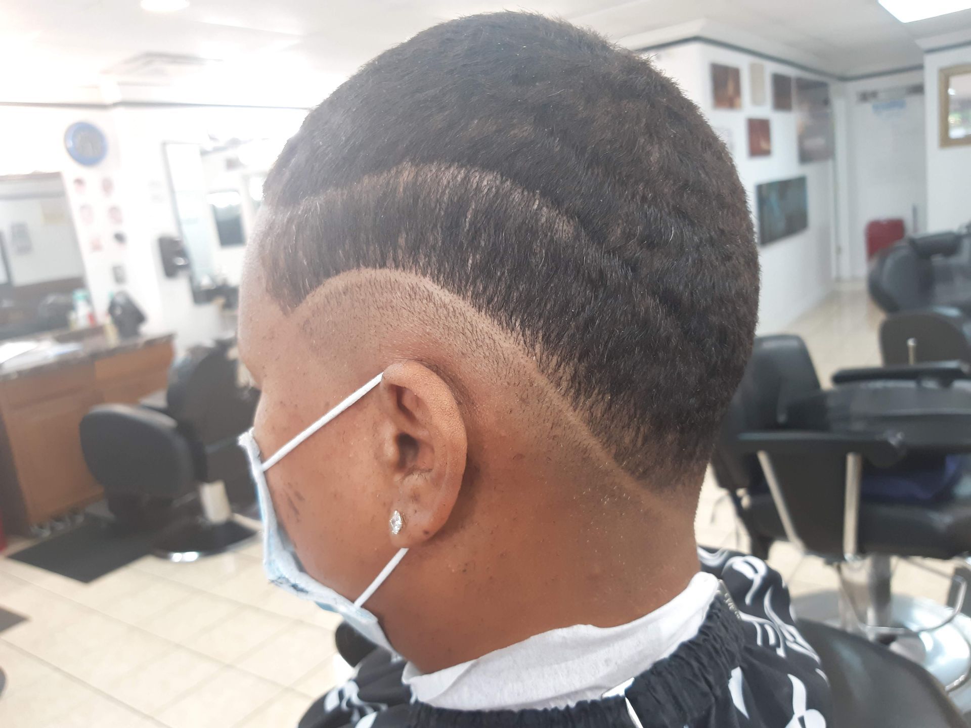 A man wearing a mask is getting his hair cut at a barber shop.