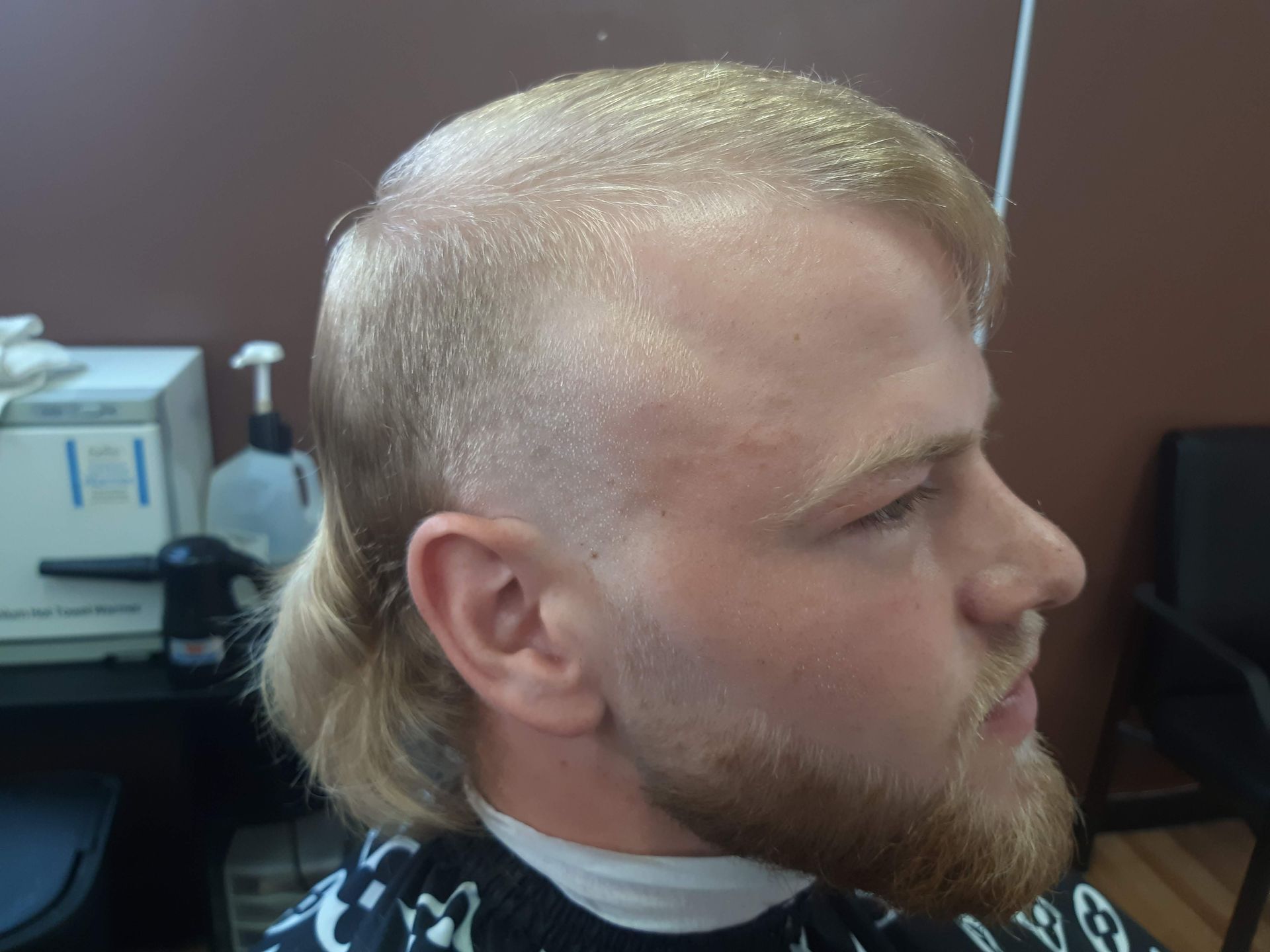 A man with blonde hair and a beard is getting his hair cut