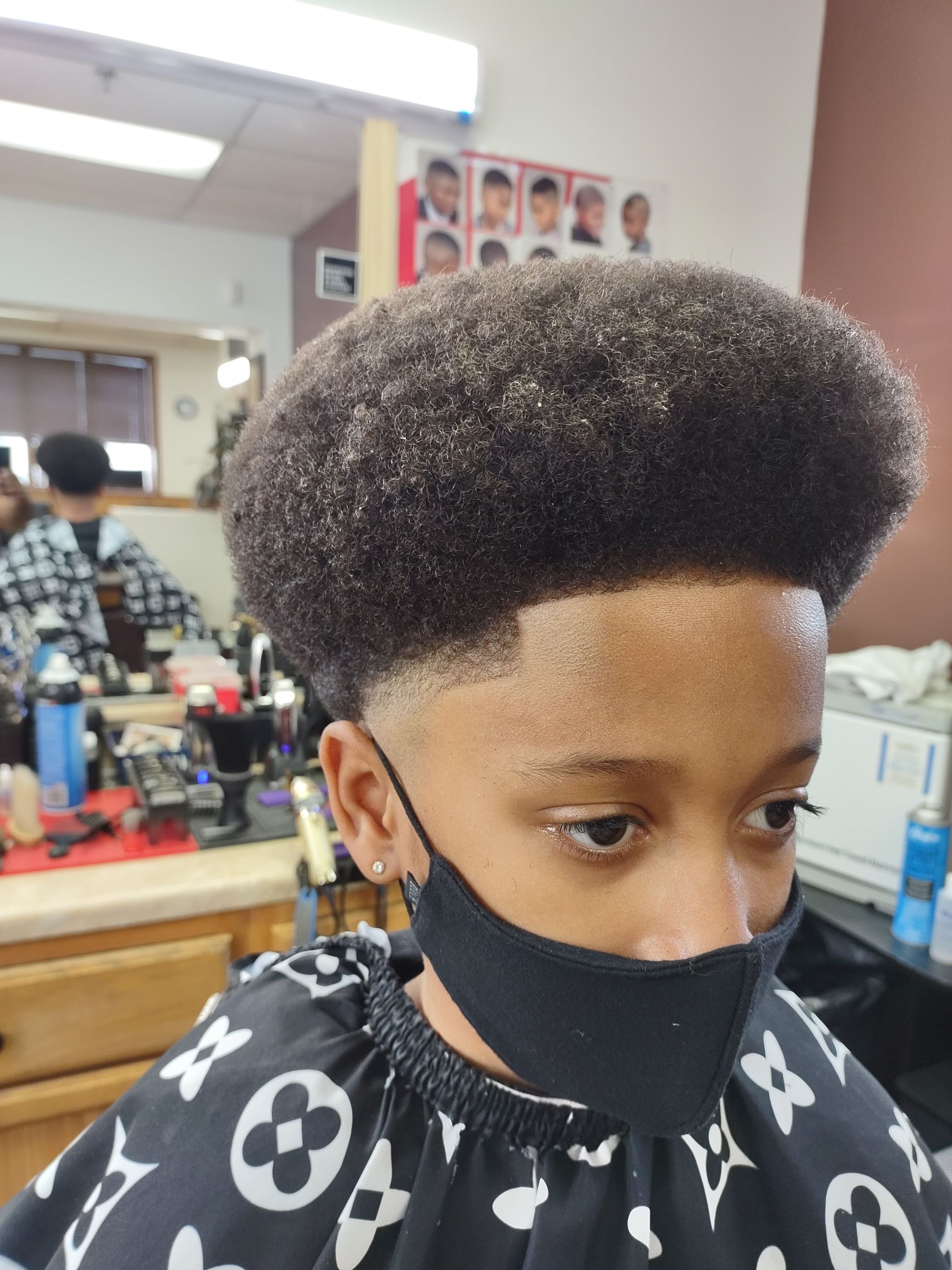 A young boy wearing a face mask is getting his hair cut at a barber shop