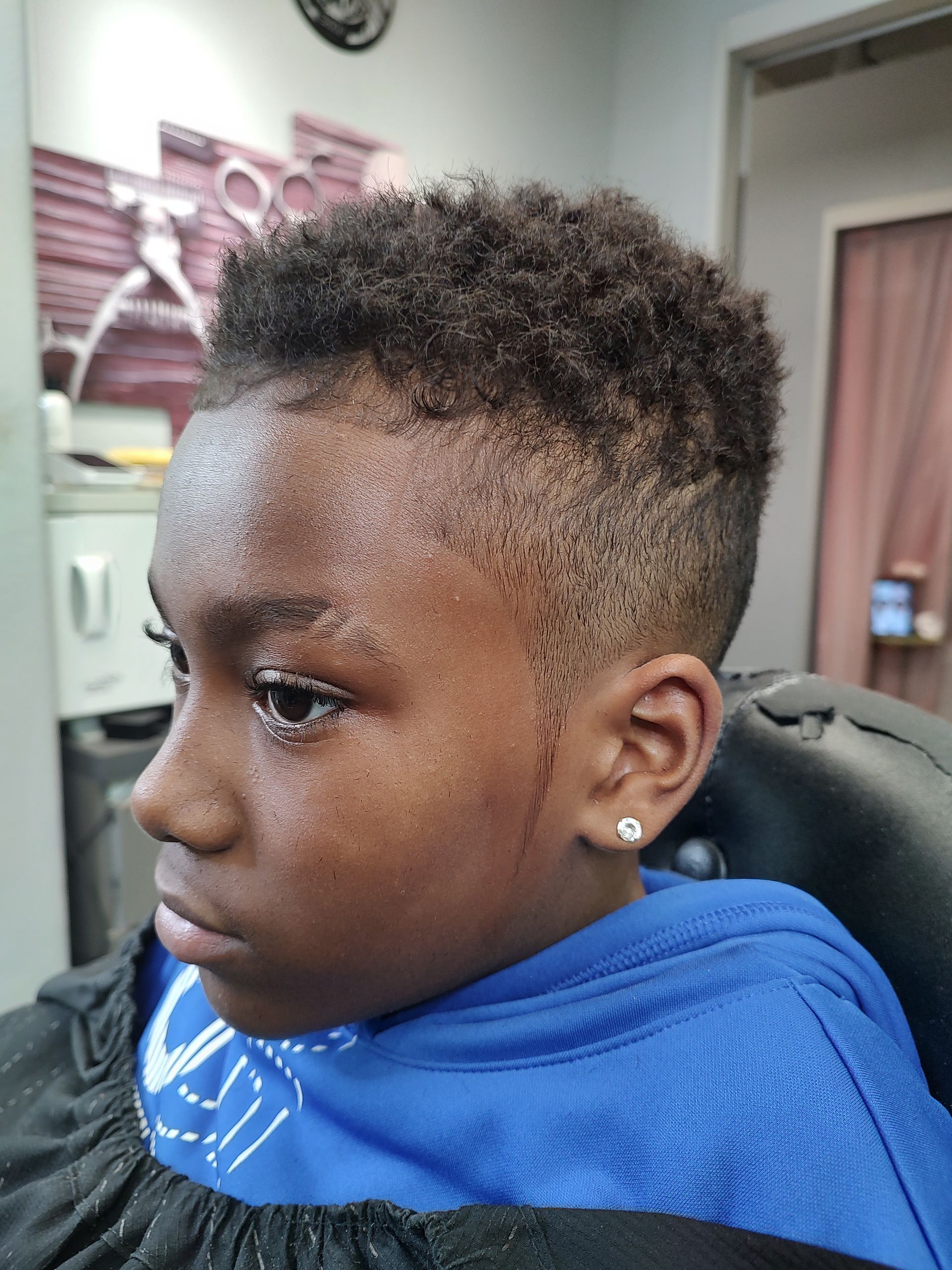 A young boy is getting his hair cut at a barber shop.