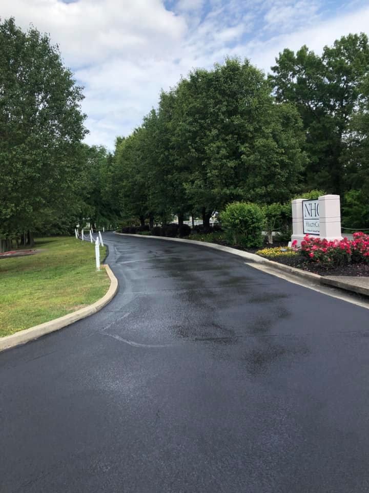 A black asphalt road surrounded by trees and bushes.
