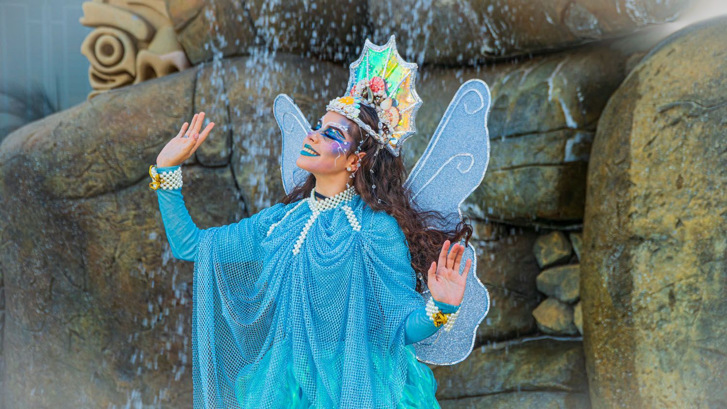Uma mulher vestida de fada está parada em frente a uma cachoeira.
