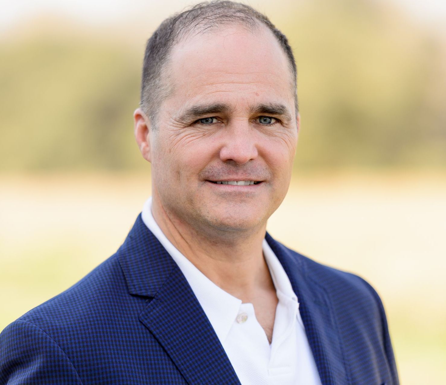 A man in a blue shirt is smiling with his arms crossed.