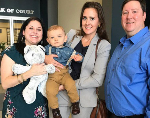 A group of people are posing for a picture with a baby and a teddy bear.