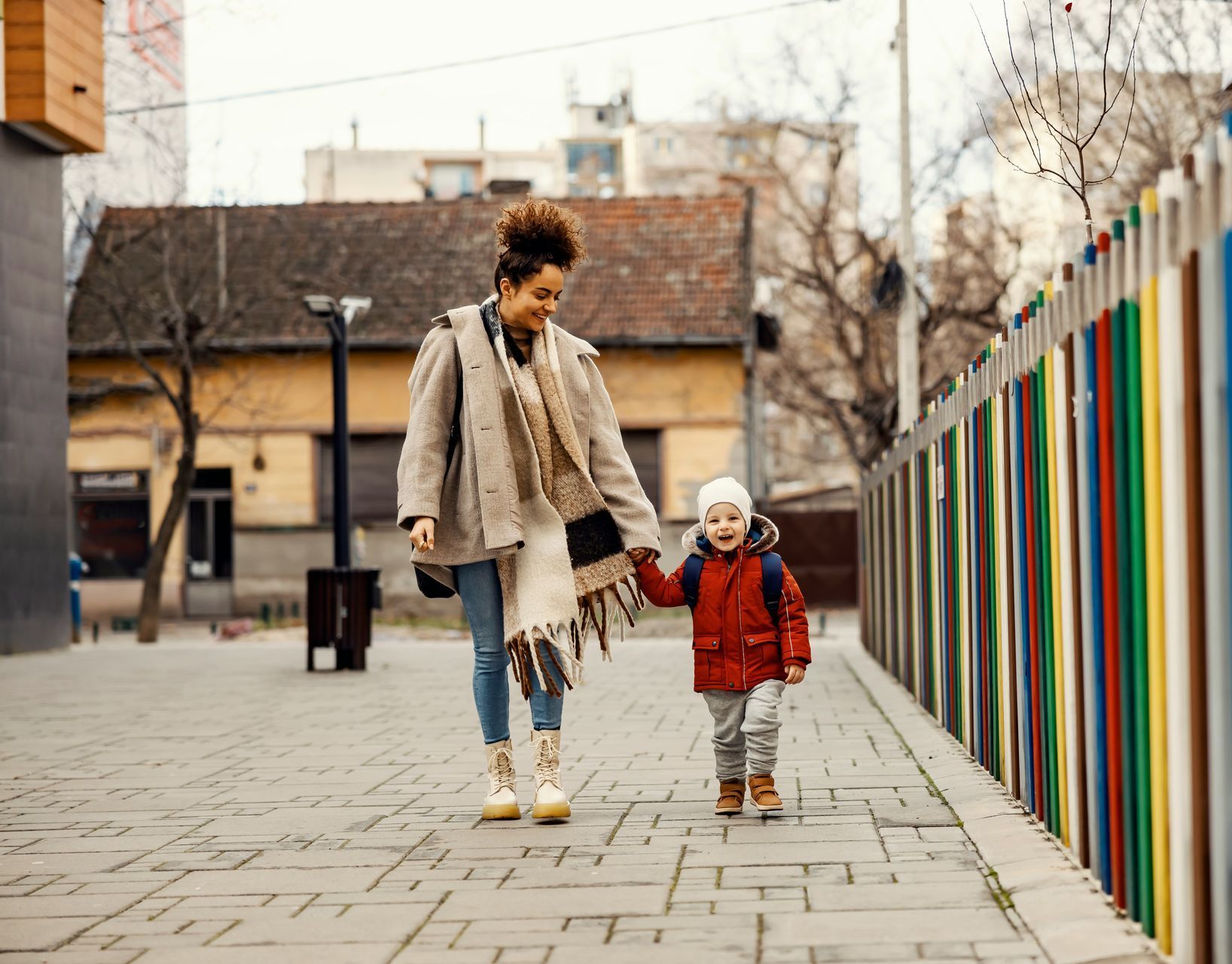 A woman and a child are walking down a sidewalk holding hands.