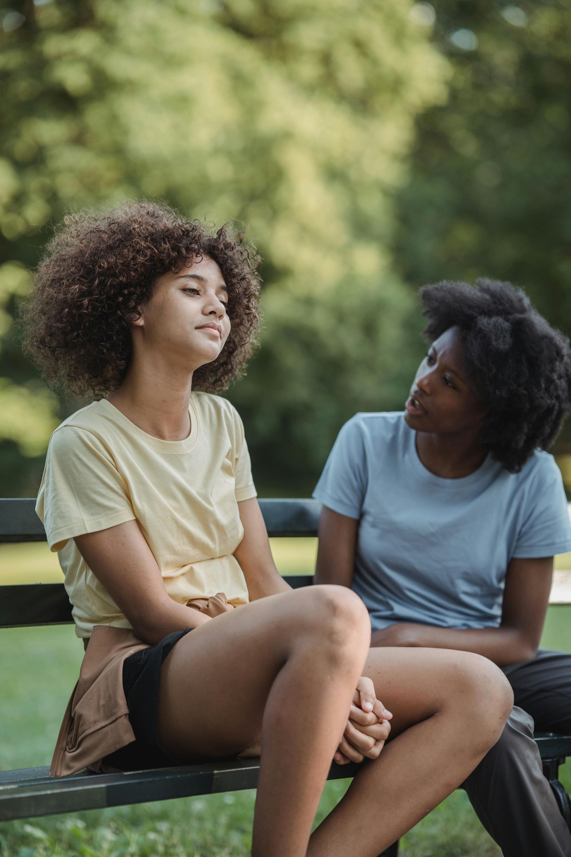 Two women are sitting on a park bench talking to each other.
