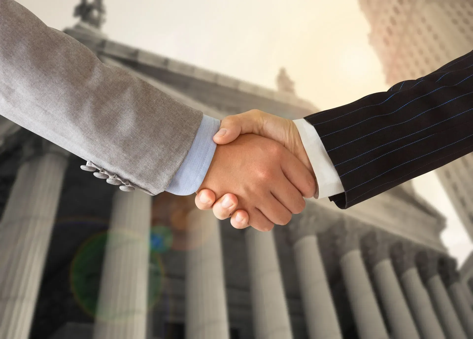 Two people in business suits shaking hands in front of a government building