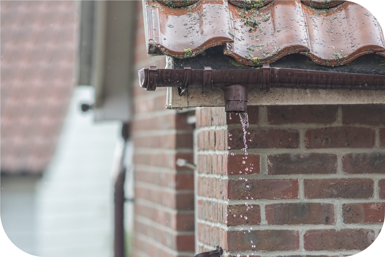 A gutter is leaking water from the roof of a brick building.