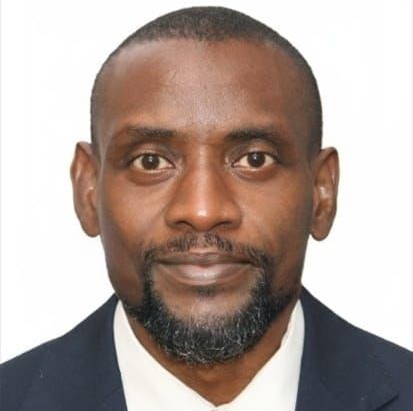 A Black man in a suit and tie, looking forward with a small smile.