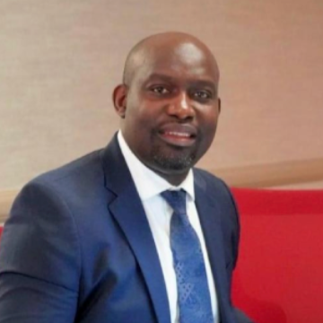 Man in a blue suit and tie, smiling, in an office setting.