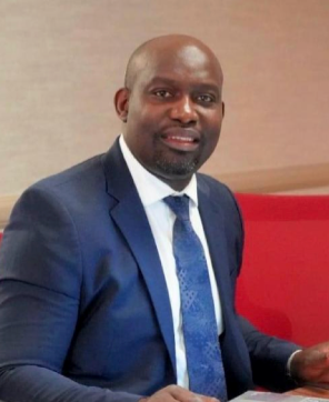 Man in a blue suit and tie, smiling at the camera.
