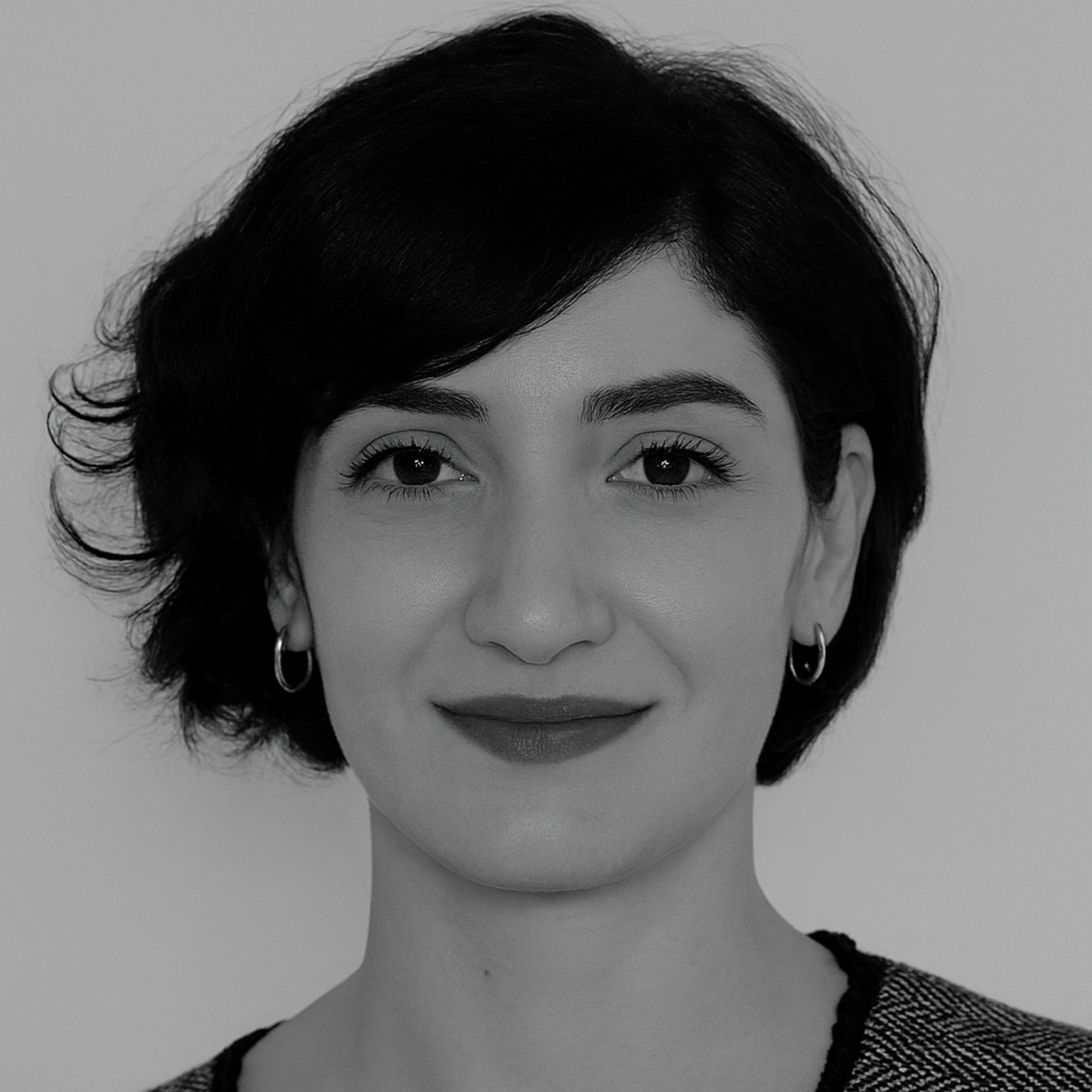 Woman with dark hair, smiling, wearing earrings, in grayscale portrait.