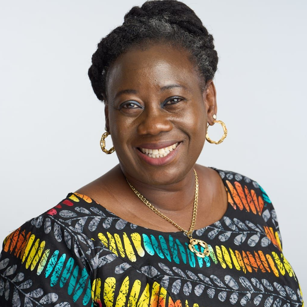 Smiling woman with dark skin, wearing a patterned top and gold jewelry.
