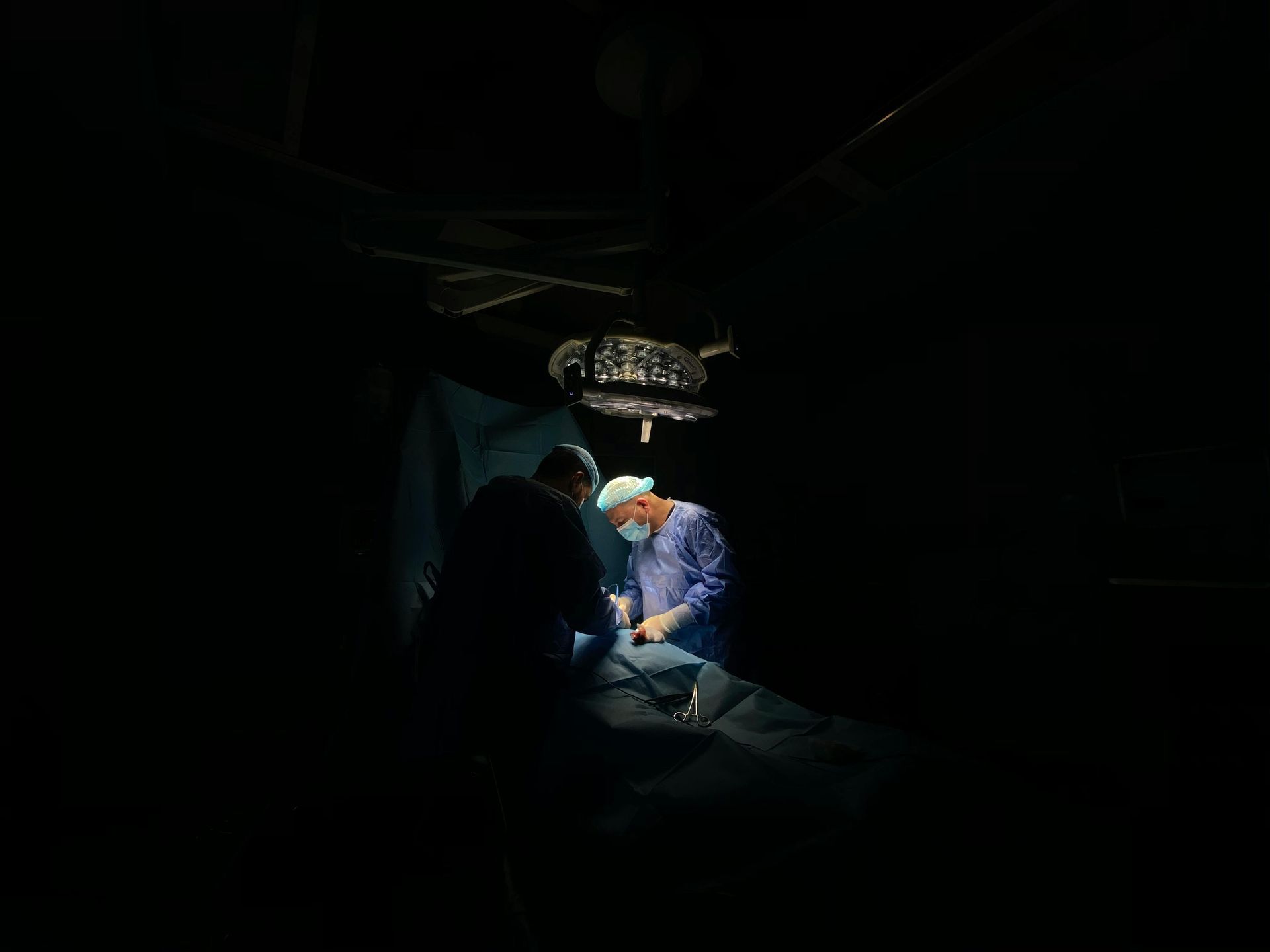 Surgeons in operating room, lit by overhead lamp, performing a procedure.