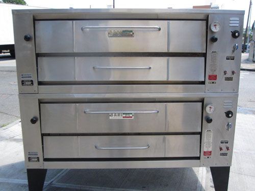 Baker placing loaves of bread into a commercial oven with a peel. Stainless steel, warm interior.