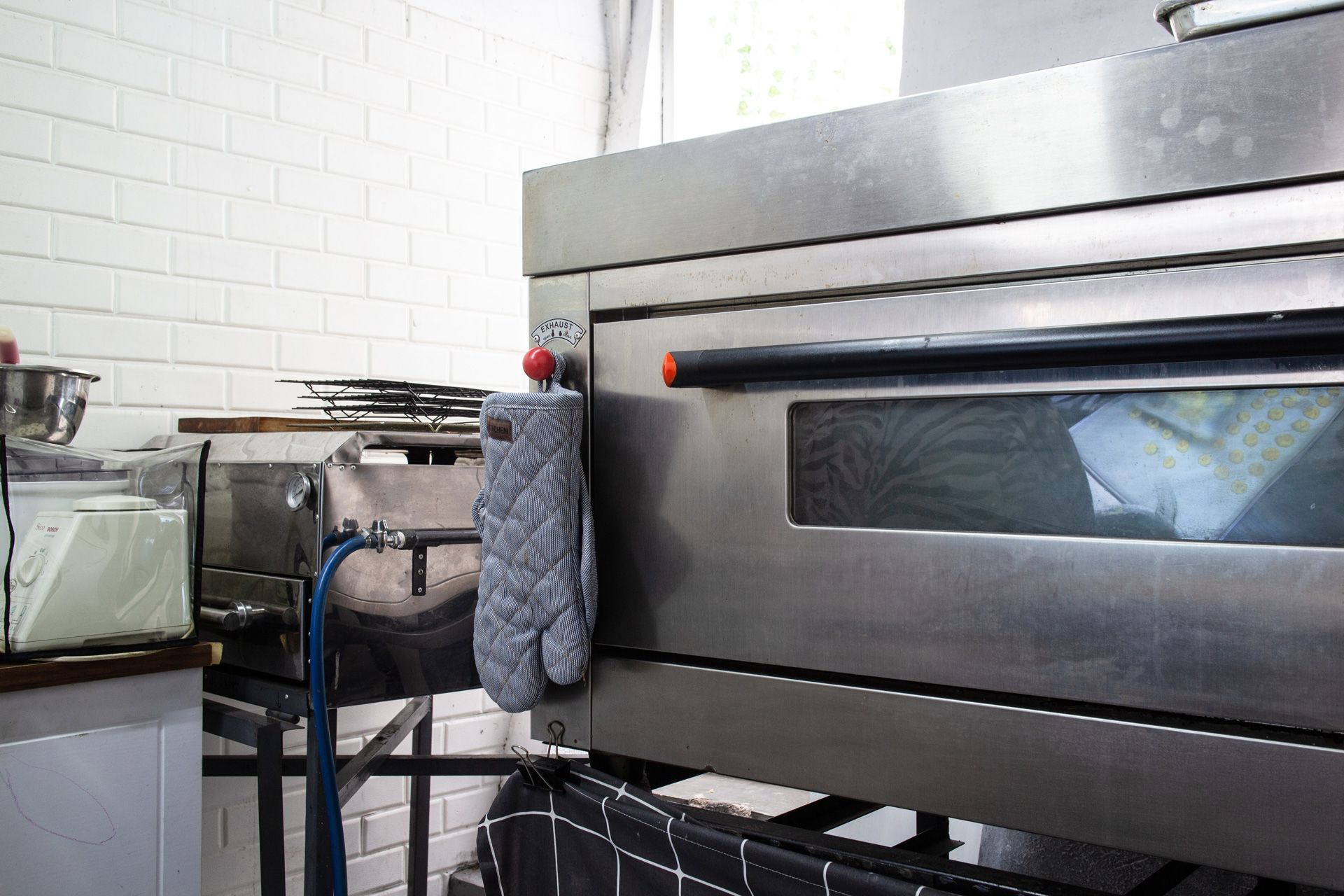 Commercial oven with a gray oven mitt hanging on the side, in a commercial kitchen.