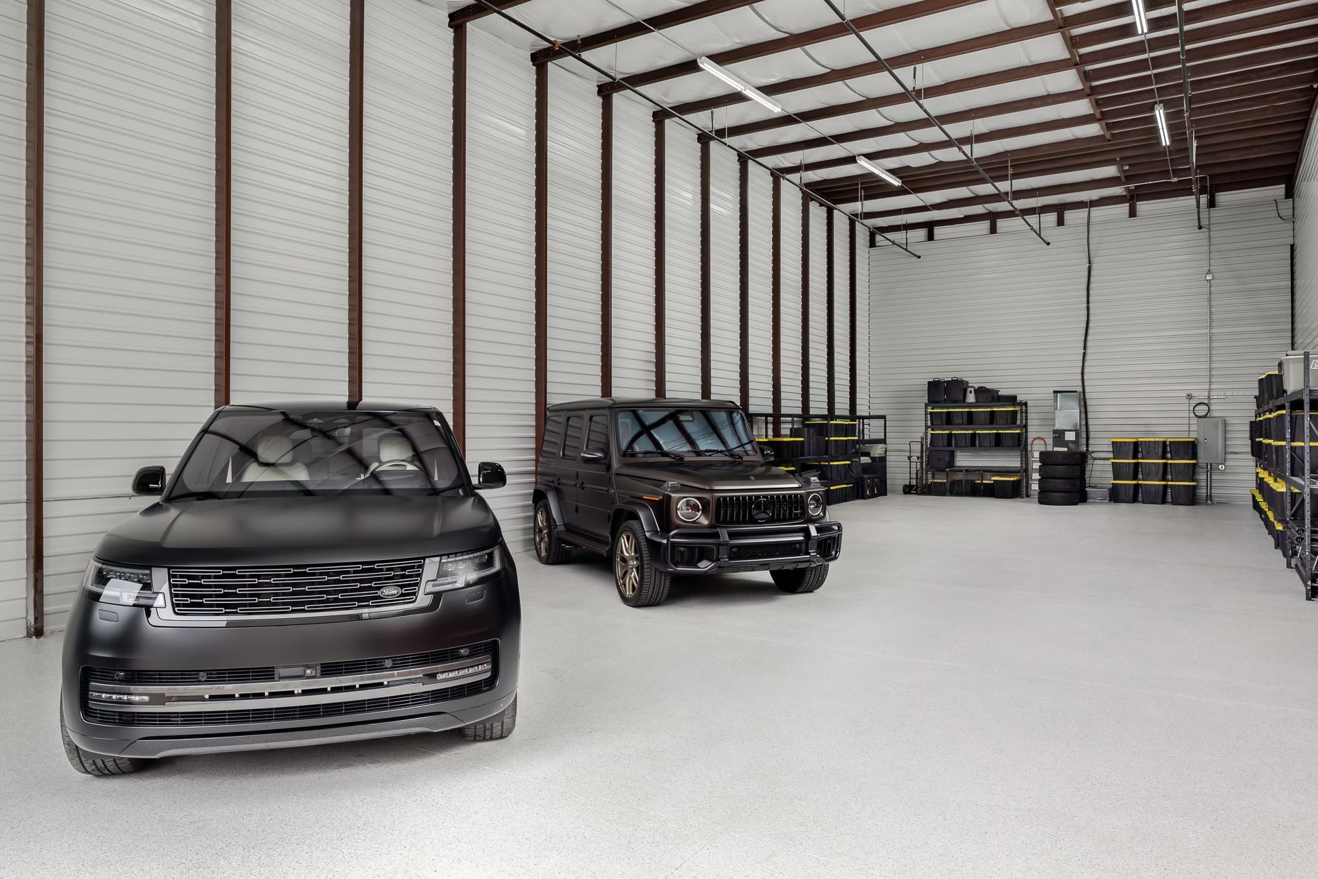 Two black SUVs parked in a large, bright storage unit with shelving.
