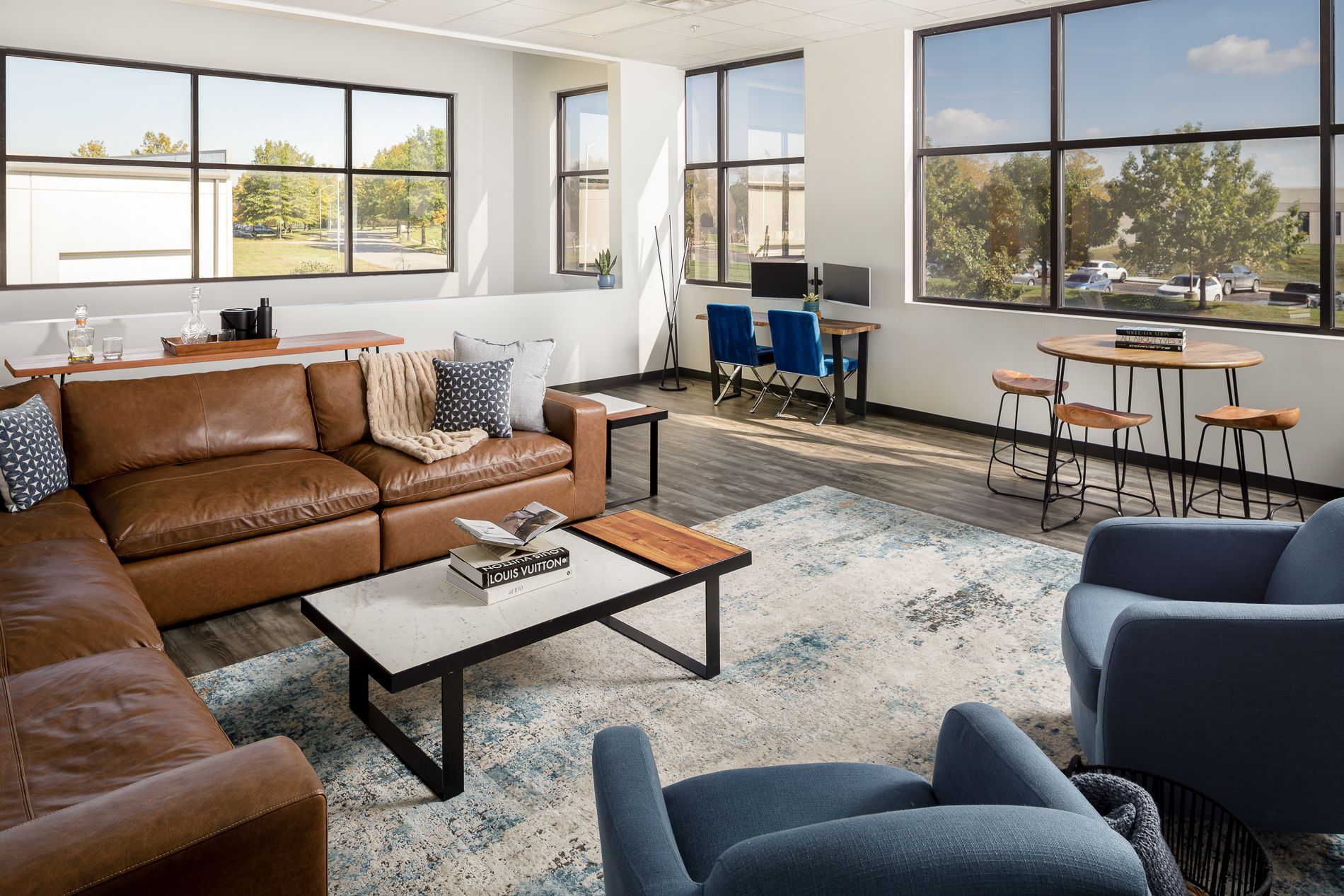 Modern office lounge with leather sectional sofa, blue armchairs, and large windows.