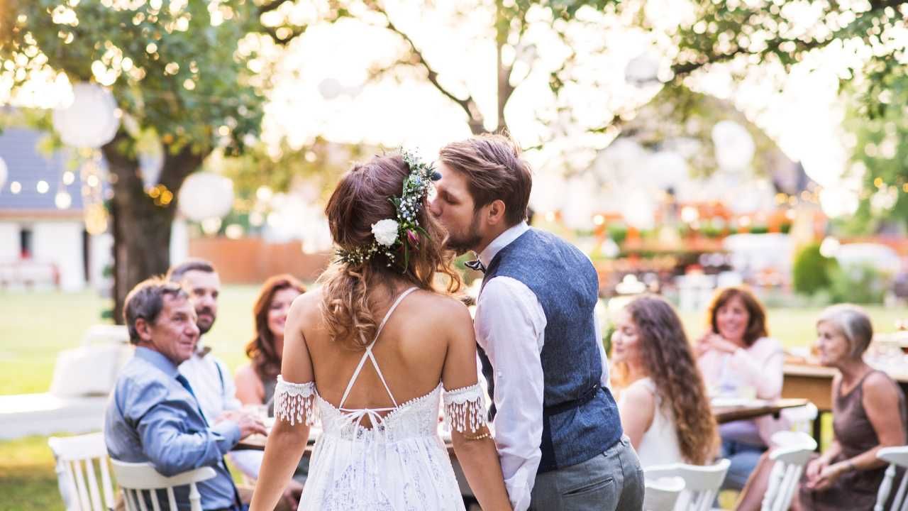 A newlywed couple shares a kiss during their outdoor wedding reception.