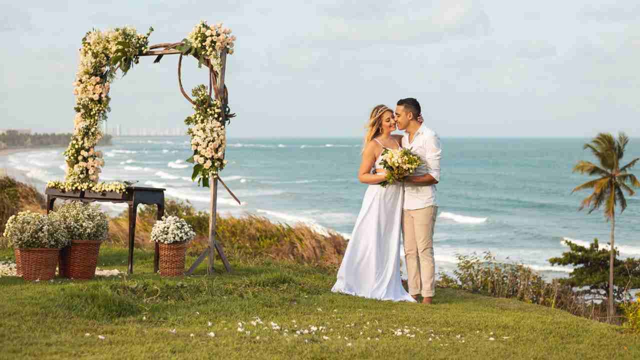 A bride and groom share a romantic kiss on a picturesque beach setting.