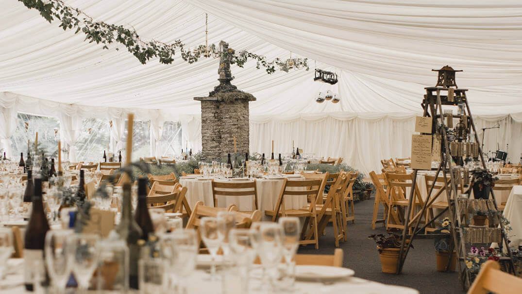 A wedding reception in a tent with decorated tables and chairs.