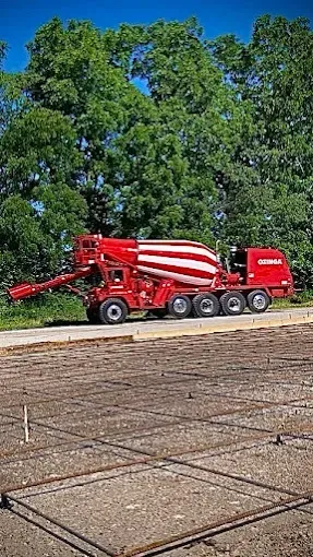 Red and white concrete mixer truck pours concrete into a prepared square on a construction site.