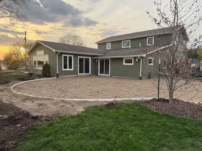 Green house with a circular gravel patio under construction; grassy foreground.