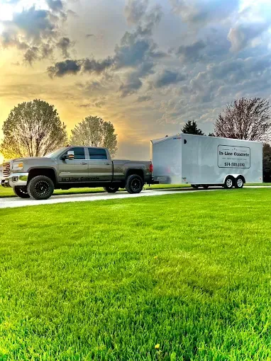 Gray pickup truck towing a white trailer on a green lawn under a cloudy sky at sunset.