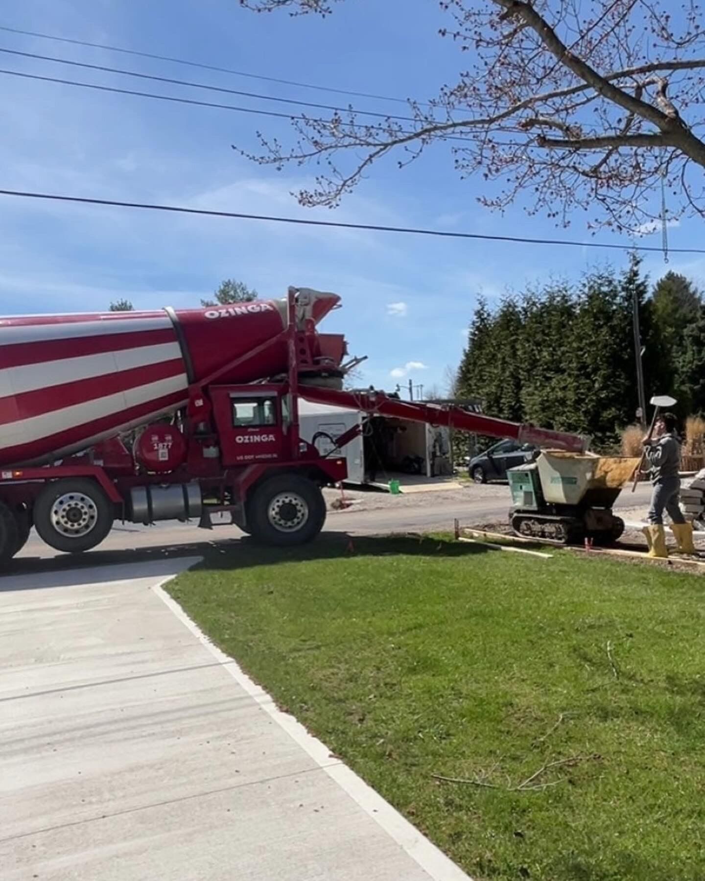 Red concrete truck pouring into a mini-dumper on a residential street.