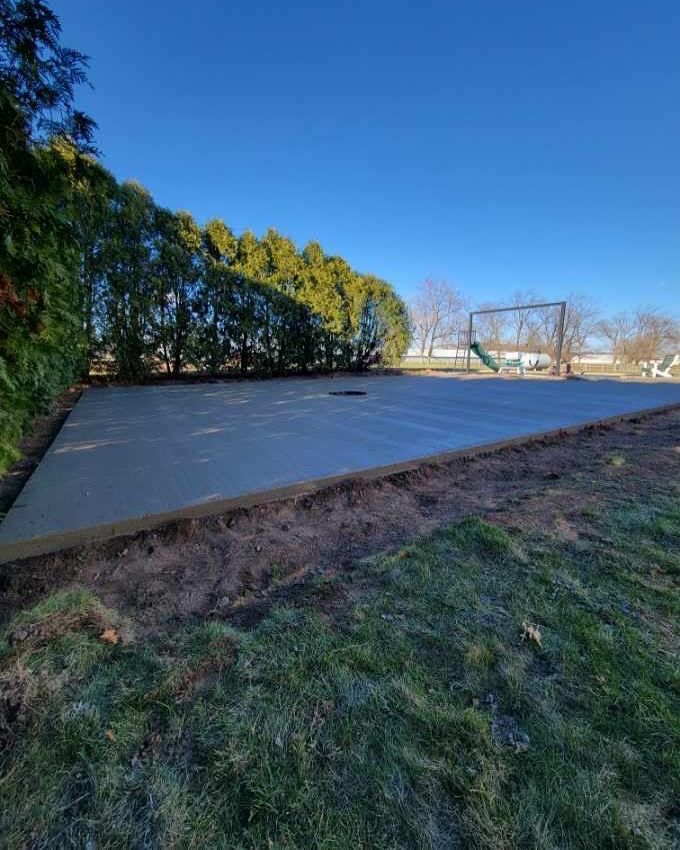 Newly poured concrete slab in a yard; a swing set is visible in the background.