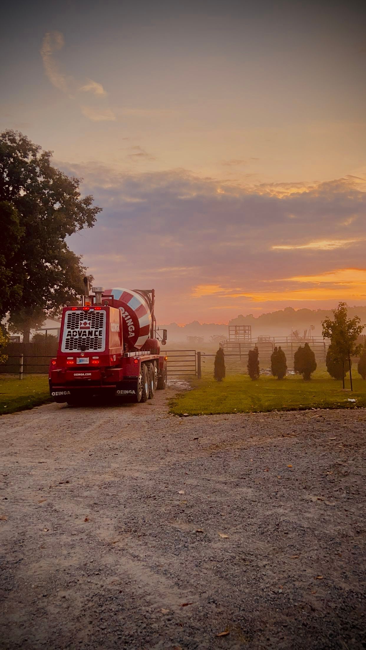 Red truck parked on gravel, facing a sunrise over a field.