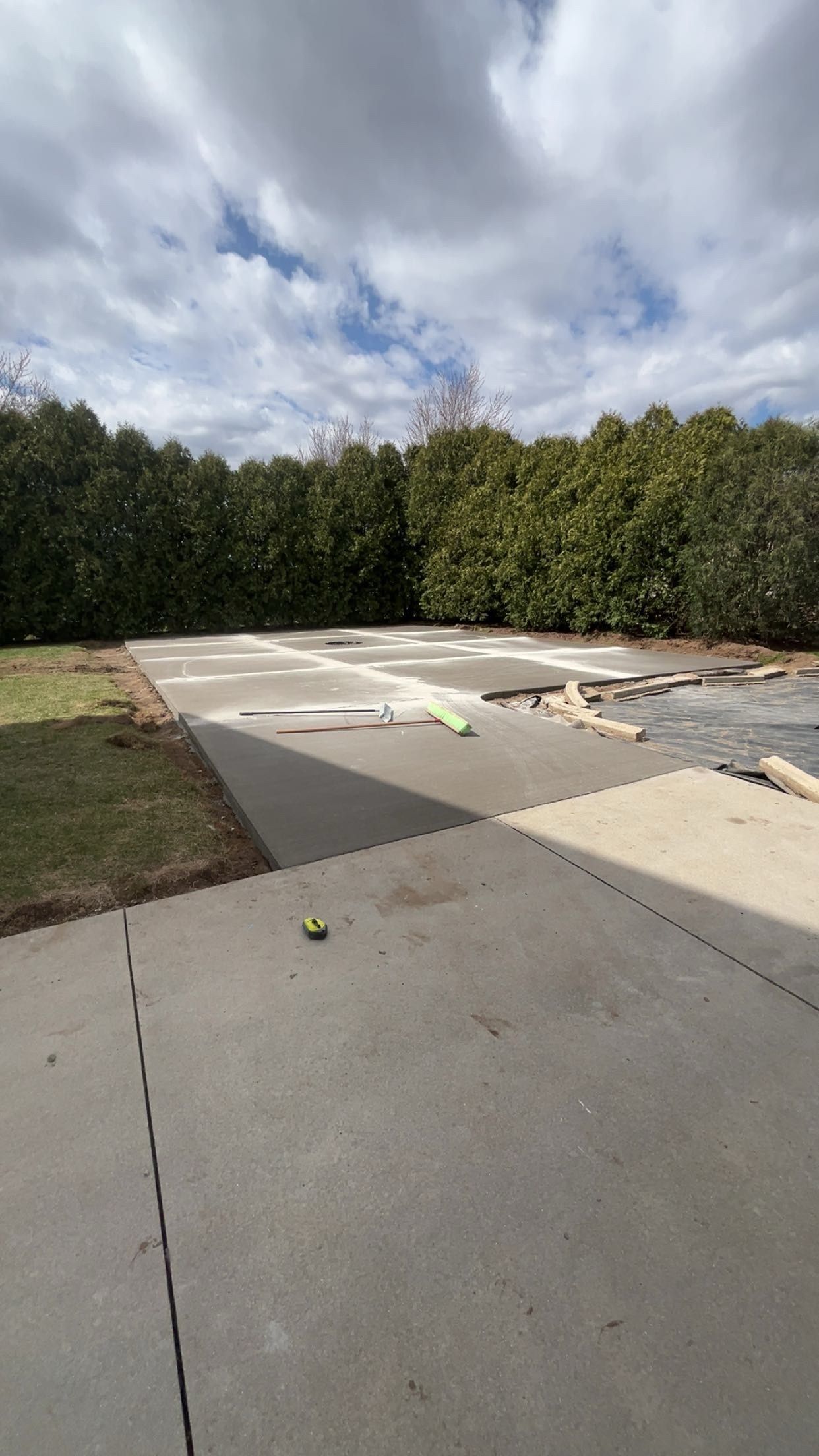 Concrete patio with dark green bushes in the background, cloudy sky overhead.