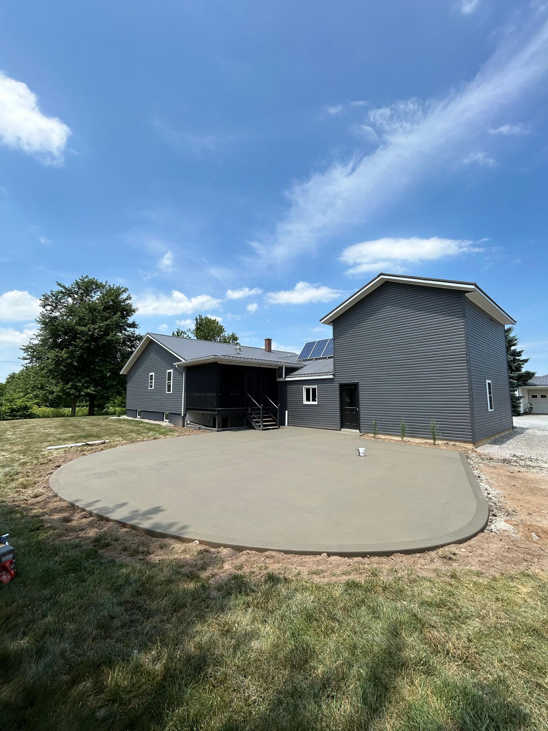Freshly poured concrete patio in front of a gray house on a sunny day.