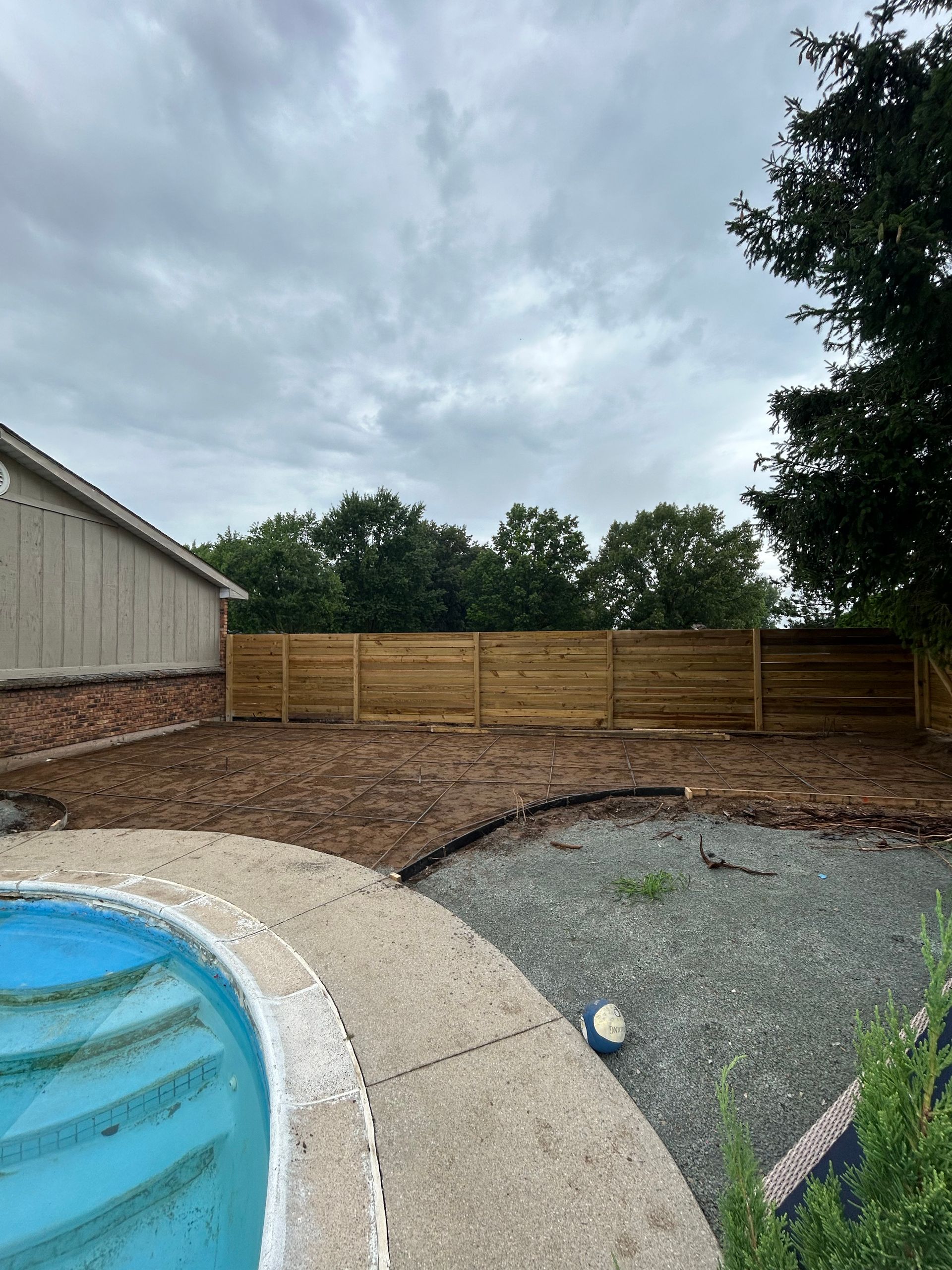 Backyard with a pool, new wooden fence, and cloudy sky.